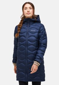 Navy blauwe pufferjas met een gestructureerd golfpatroon, volledige rits, capuchon en lange mouwen. Bevat het Peak Performance-logo op de borst en het mouw.