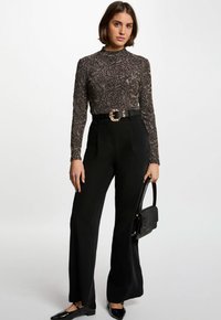 Pantaloni neri a vita alta abbinati a un top aderente a maniche lunghe con design floreale metallico e una cintura con fibbia circolare dorata.