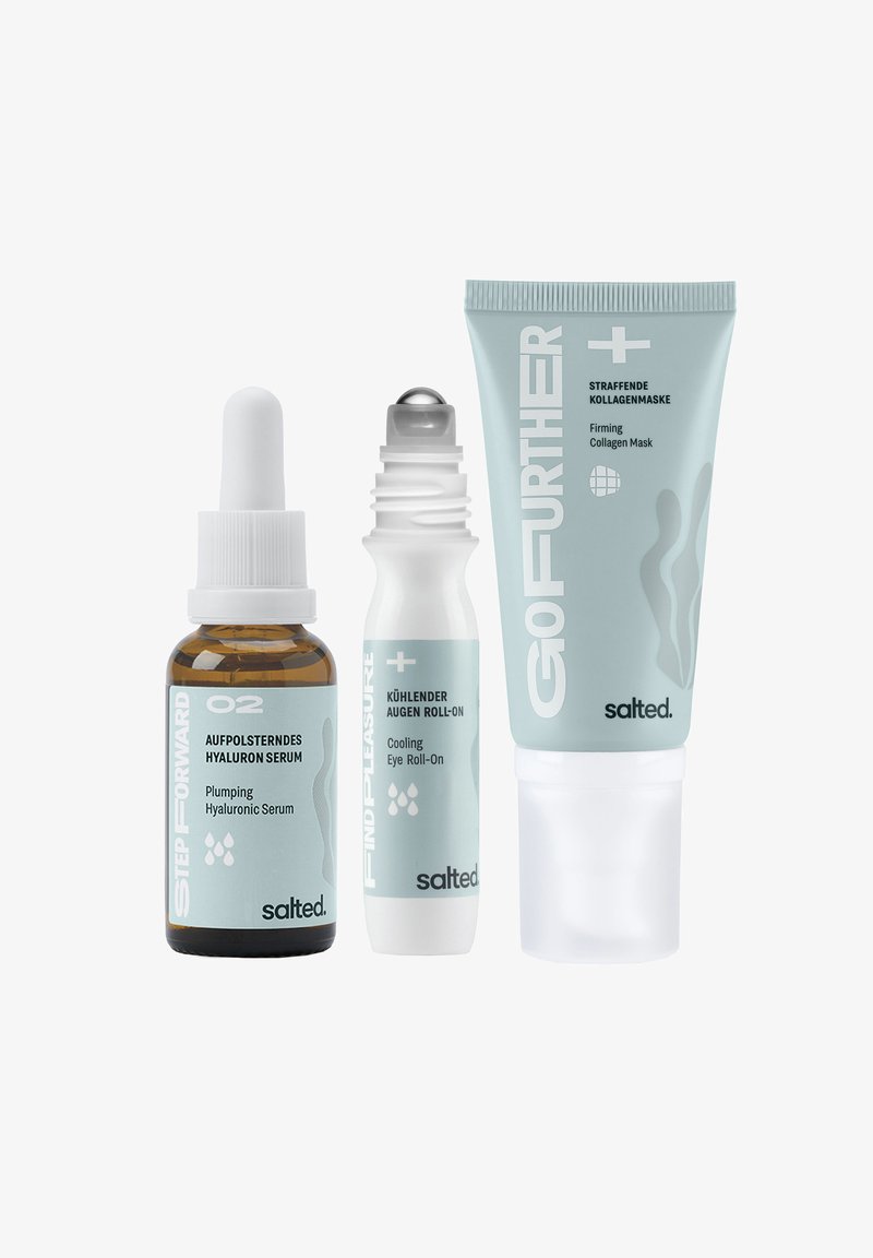 Trois produits de soins de la peau : un flacon compte-gouttes en verre brun, un roll-on blanc et un tube blanc. Tous portent des étiquettes bleu pastel avec du texte.