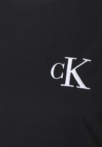 Svart bomullströja med vitt broderat "cK"-logotyp på vänster bröstområde. Slät textur med klassisk rundhalsdesign.