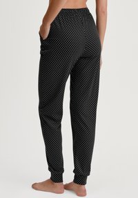 Zwarte joggers met polka dots, gemaakt van zachte stof, met een elastische tailleband, zijzakken en taps toelopende boorden bij de enkels.