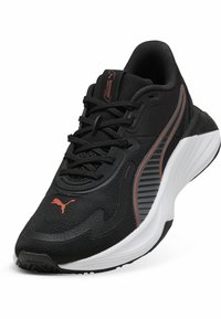 Chaussure de sport noire en textile et caoutchouc, avec une semelle blanche, des accents texturés et un logo rouge. Design à lacets avec col rembourré.