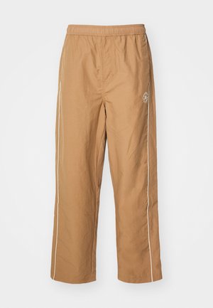 Pantaloni relaxați de culoare bej, confecționați dintr-un material ușor, având un brâu elastic și dungi laterale albe cu un detaliu mic cu logo pe picior.