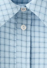 Lichtblauw geruit overhemdkraag met twee lichtbeige knopen vastgemaakt in de centrale sluiting.