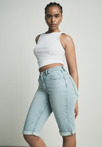 Biele pruhované crop top tričko v kombinácii so svetlomodrými denimovými bermudami s vysokým pásom, s ohrnutými okrajmi a mierne roztrhnutou textúrou.