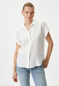 Witte, kortärmige shirt met een knoopsluiting, gemaakt van textuurstof. Lichtgewicht met opgerolde mouwen en een ontspannen pasvorm.