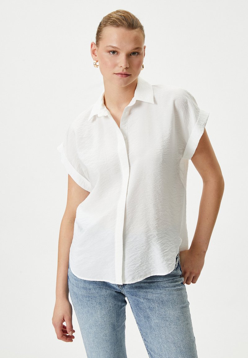 Witte, kortärmige shirt met een knoopsluiting, gemaakt van textuurstof. Lichtgewicht met opgerolde mouwen en een ontspannen pasvorm.