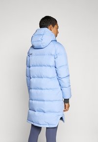 Piumino azzurro chiaro con cappuccio, caratterizzato da sezioni a quadri orizzontali e polsini a costine. Logo visibile sulla parte superiore della schiena.