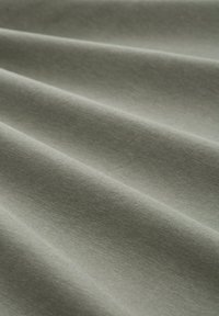 Hellgrüner Stoff mit glatter Textur, der weiche Falten und einen dezenten Glanz auf der Oberfläche aufweist, was sein feines Gewebe hervorhebt.