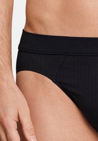 Sorte herrebriefs med ribbet tekstur og elastisk talje. Nærbillede viser syninger og en tætsiddende pasform.