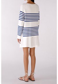 Pull rayé en crème avec des rayures horizontales bleues ; manches longues ; associé à une jupe blanche et des sandales à lanières ; texture lisse.