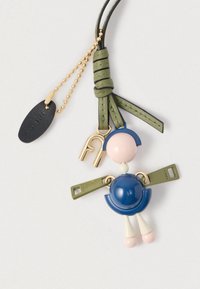 Kľúčenka zobrazujúca modrú a ružovú postavu s okrúhlou hlavou a sukňou, zvýraznenú zelenými remienkami a zlatým kovaním. Použité sú textúrované materiály.