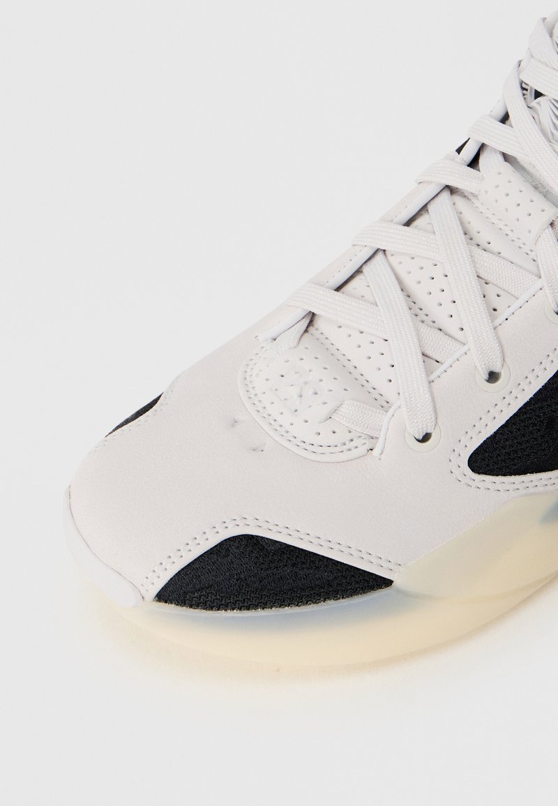 Zapatilla con una parte superior sintética blanca y acentos negros, detalles texturizados y una suela de goma translúcida; incluye cordones planos.