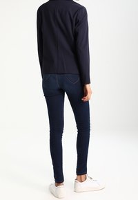 Námořnický modrý strukturovaný blejzr se štíhlým střihem, kombinovaný s tmavými džíny skinny a bílými teniskami. Hladká tkanina a minimalistický design.