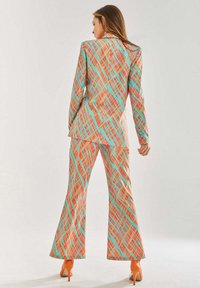 Multicolored suit featuring a geometric pattern in orange, turquoise, and pink, with a fitted jacket and flared pants; paired with orange heels.