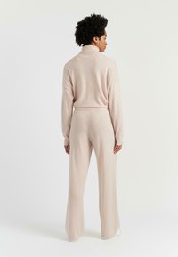 Completo a due pezzi in morbido knit rosa chiaro, composto da un pullover con collo alto e pantaloni a gamba larga, caratterizzato da una vestibilità comoda e maniche lunghe.