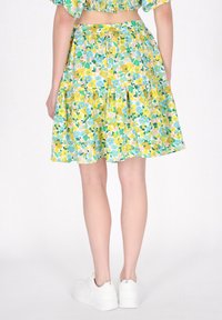 Gonna con stampa floreale in giallo, blu e verde. Presenta un design a strati e una vita elasticizzata. Abbinata a sneakers bianche.