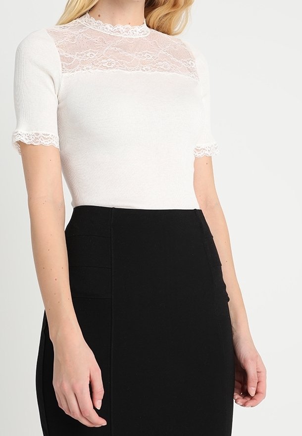 Top blanco de manga corta con detalle de encaje en el escote y las mangas, combinado con una falda negra ajustada con pliegues laterales.