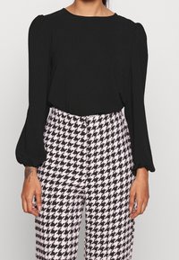 Svart långärmad blus med puffiga axlar, i kombination med högmidjade byxor med svart och vit hundtandsmönster.