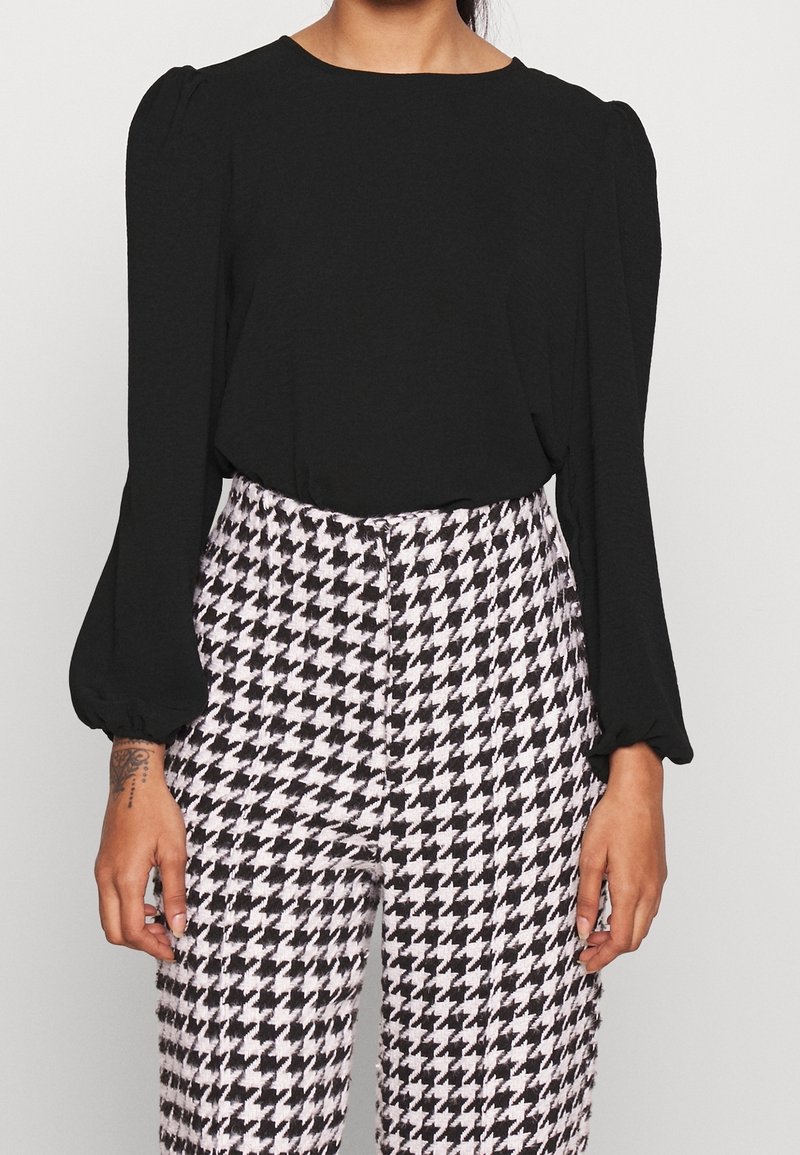 Svart långärmad blus med puffiga axlar, i kombination med högmidjade byxor med svart och vit hundtandsmönster.