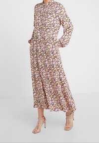 Lång, knäppt klänning med ett rosa och beige bladmönster. Har krage, långa ärmar och sidfickor. Bärs med beige remklackar.