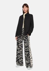 Black shirt with a tailored design, paired with wide-leg trousers featuring a black and white zebra print. Silver sneakers complete the look.