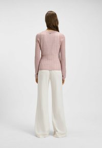 Top a maniche lunghe di colore rosa chiaro in maglia, con motivo a zigzag e scollatura arrotondata, abbinato a pantaloni bianchi a gamba larga e design minimalista.