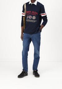 Navy long-sleeve polo shirt with white collar and red accents, featuring "Tommy Jeans" logo; blue denim jeans and black sneakers.