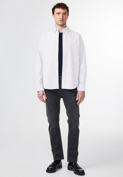 Hvid skjorte med krave, båret over en mørkeblå skjorte. Kombineret med mørkegrå jeans og sorte lædersko.