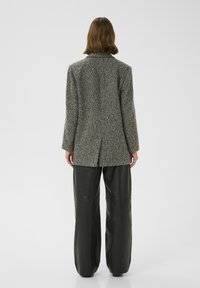 Grijze textuurblazer met een geknipt kraag, enkele rugventilatie en lange mouwen, gecombineerd met hoog-waist zwarte leren wijde broek.