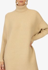 Pull à col roulé beige côtelé avec une coupe décontractée et des manches longues. Présente un tissu texturé pour plus de chaleur et de style.