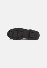 Black rubber shoe sole with a textured surface, featuring multi-directional grooves and a reinforced heel for traction and durability.