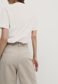 Hvid kortærmet t-shirt parret med beige skræddersyede bukser. Bukserne har baglommer og en glat finish. Enkel og moderne design.