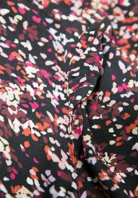 Czarna tkanina z rozproszonym, abstrakcyjnym wzorem kwiatowym w odcieniach różu, pomarańczu, kremu i brązu o gładkiej, lekkiej fakturze.