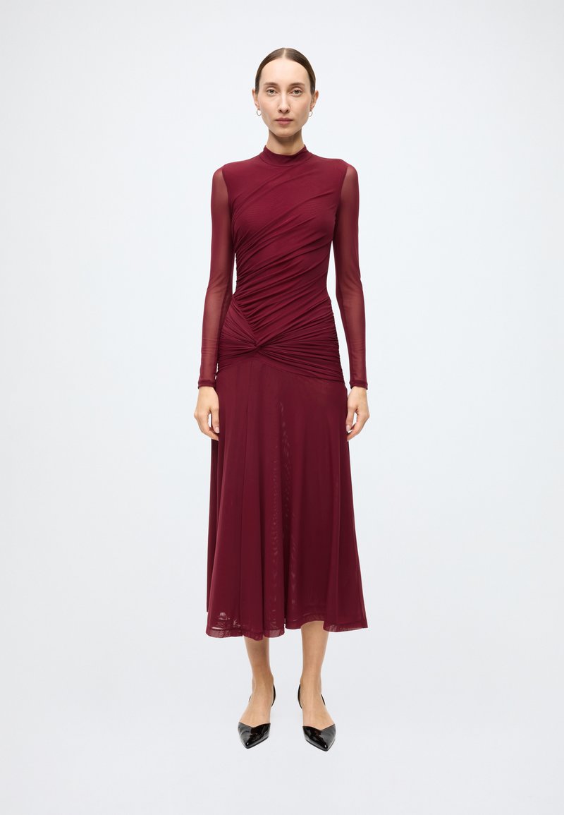 Burgundy dress with long sheer sleeves, fitted bodice, and flowing skirt. Textured fabric with gathered details at the waist and torso.