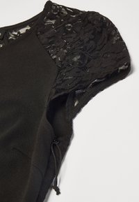 Schwarzes Kleid mit einem glatten Stoffkörper und aufwendigen transparenten Spitzenärmeln mit floralen Mustern. Enthält einen seitlichen Reißverschluss und einen verstellbaren Kordelzug.