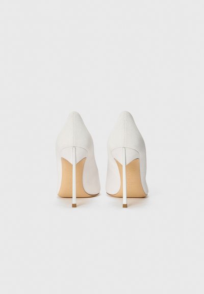 White high-heeled shoes with a pointed toe design, textured fabric upper, and a slender metallic heel. Light tan sole with embossed branding details.