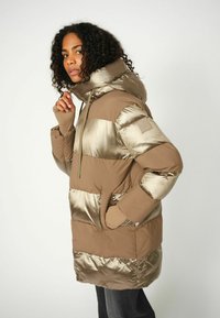 Gewatteerde jas in lichtbruin met glanzende beige strepen, voorzien van een capuchon, ritssluiting aan de voorkant en duimgatovergangen, gemaakt van een glad synthetisch materiaal.