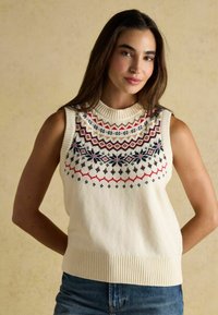 Bez piedurknēm krēmkrāsas džemperis ar ribotu apkakli un apakšmalu, noformēts ar krāsainu zviedru paraugu sarkanā, zilā un melnā krāsā krūtīs.