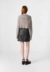 Cropped grey knitted sweater with open weave details, paired with a black leather mini skirt. Footwear features chunky block heels.