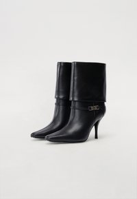 Bottines en cuir noir avec des bouts pointus, des talons hauts et un design à revers. Comprend une fine sangle avec des détails métalliques.