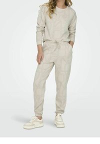 Svetle béžový soubor loungewear, který zahrnuje dlouhý rukáv top s geometrickými liniovými vzory a odpovídající zúžené kalhoty s elastickým pasem a manžetami.