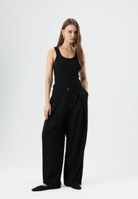 Débardeur noir côtelé associé à un pantalon noir taille haute à jambes larges, doté de poches latérales et d'une ceinture avec une boucle argentée.