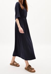 Laivastonsininen, lyhythihainen maksimekko jossa on joustava vyötärö, yhdistettynä ruskeisiin liukukengiin, joissa on leikkausaukkoja.