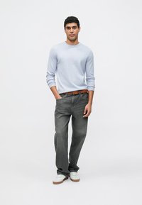 Hellblaues Langarmhemd, graue Jeans aus Denim, brauner Gürtel, weiße Turnschuhe. Stehende Figur zentriert vor neutralem Hintergrund platziert.