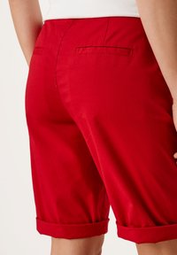 Pantalones cortos de algodón rojo con puños enrollados, que cuentan con dos bolsillos traseros y una textura suave, diseñados para un ajuste informal.