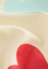 Tessuto di cotone con base crema e grandi motivi a cuore rossi e azzurri chiari. Texture morbida, superficie liscia con leggero lucido.