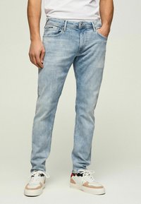 Jeans de mezclilla de un azul claro con corte ajustado, que cuentan con bolsillos delanteros y cierre de cremallera. Combinados con zapatillas blancas y beige.