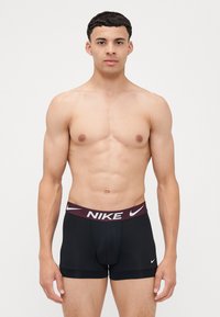 Zwarte Nike boxershorts met een bordeauxrode tailleband en witte logo-tekst. De stof ziet er glad en nauwsluitend uit, met minimale naden.