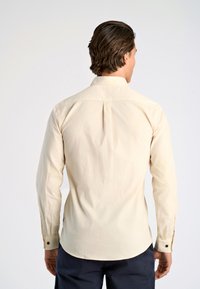 Lichtbeige langslabige shirt met een klassieke kraag, een rugplooien en knoopmanchetten, gemaakt van een soepel stof met een zachte textuur.